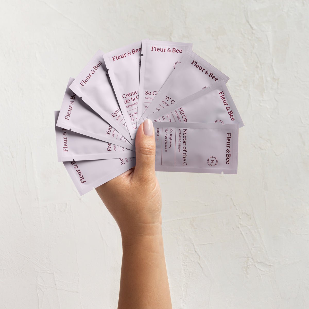 Hand holding multiple Fleur & Bee product packets against a light background